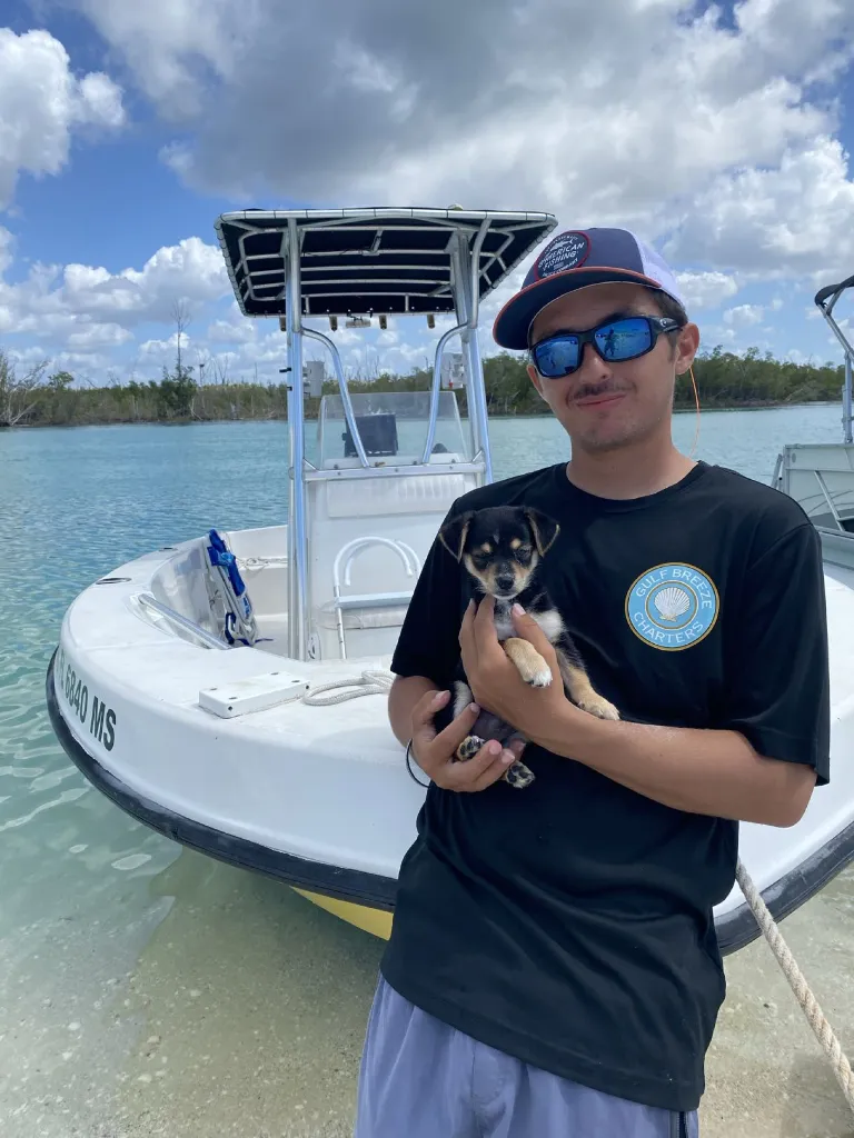 Capt. Stan Schira holding a puppy in front of his charter boat on the Southwest Florida water